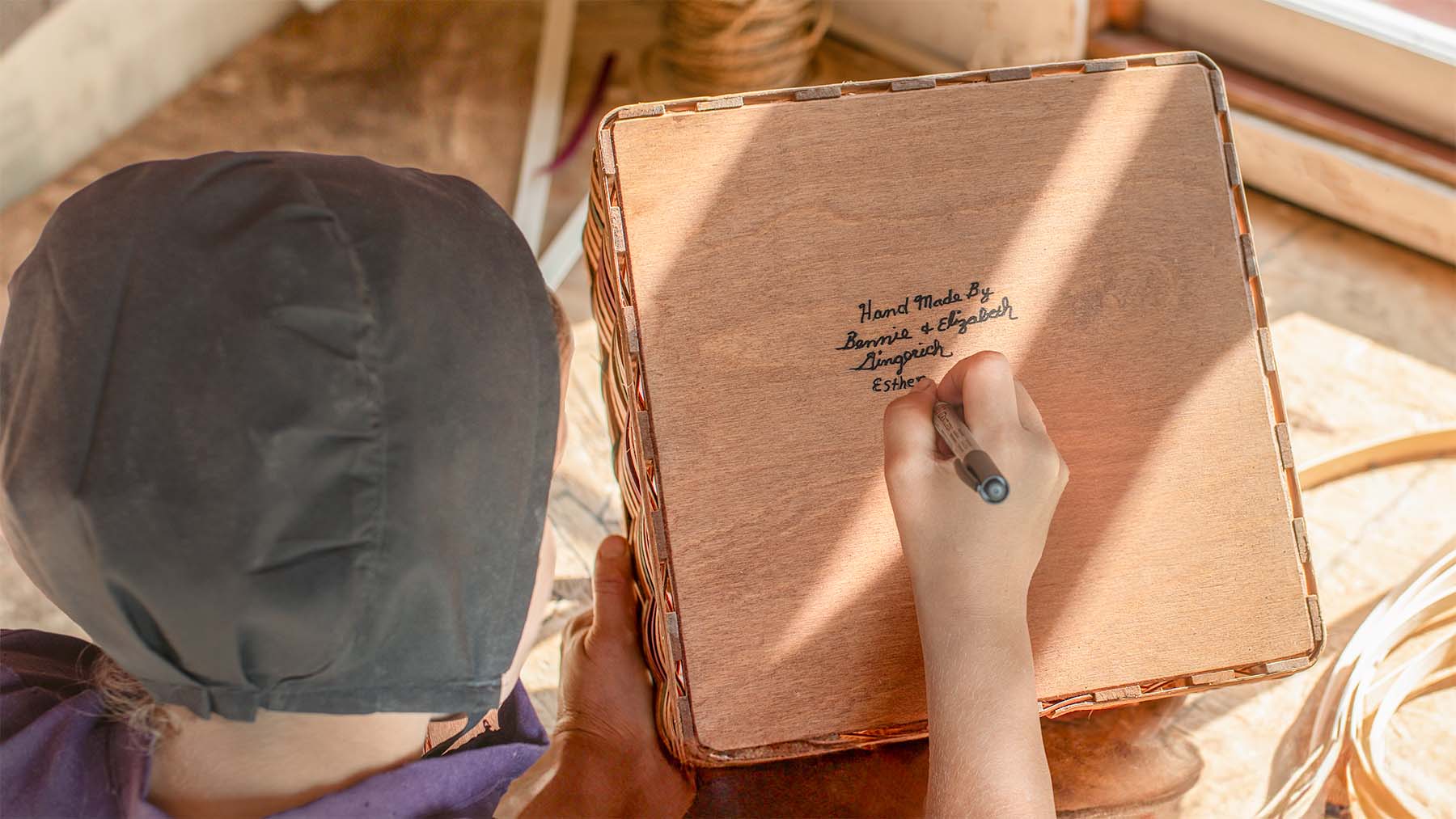 Amish crafter signing the bottom of a handwoven basket